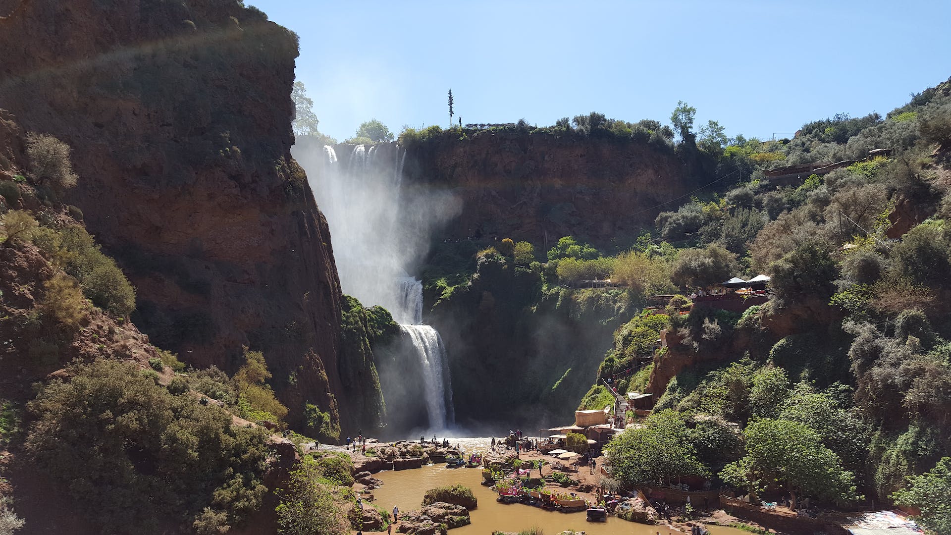 Image of the Ouzoud Waterfalls in Morocco, showcasing the stunning cascades surrounded by lush greenery and red cliffs, creating a picturesque natural setting in the Atlas Mountains